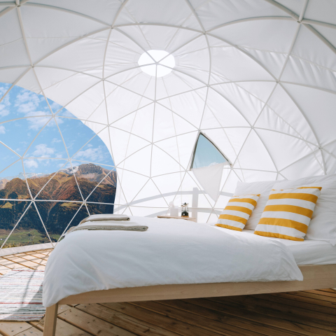 Gemütlicher Glamping-Dome mit Bett und Blick auf sonnige Berglandschaft