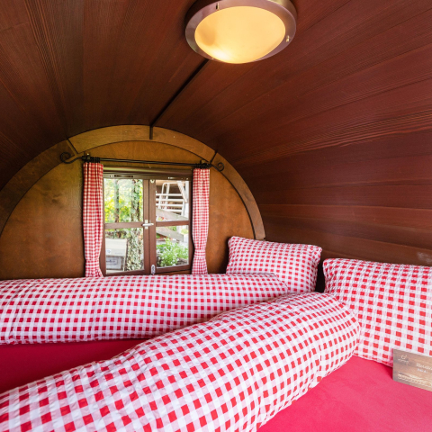 Innenansicht eines Schlaf-Fasses mit Doppelbett und karierten Kissen in Maienfeld