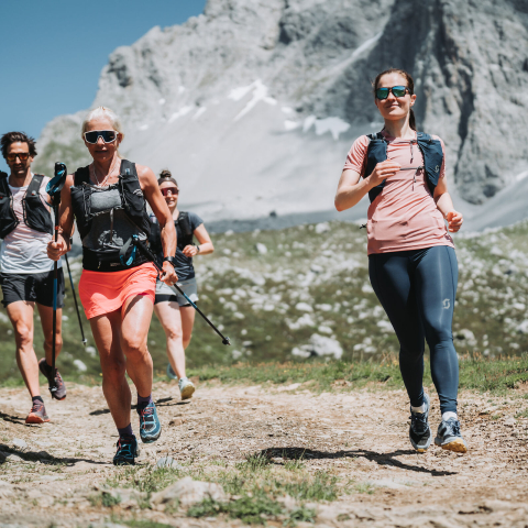 Vier Trailrunnerinnen und Trailrunner laufen auf einem Schotterweg im Rätikon vor einer felsigen Bergkette im Prättigau
