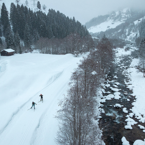 Zwei Personen beim Langlaufen auf einer Loipe am Bachufer in Disentis.