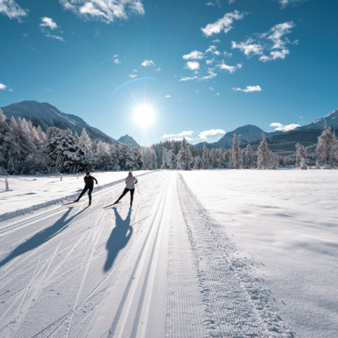 Zwei Personen beim Langlaufen auf einer sonnigen Loipe im Engadin