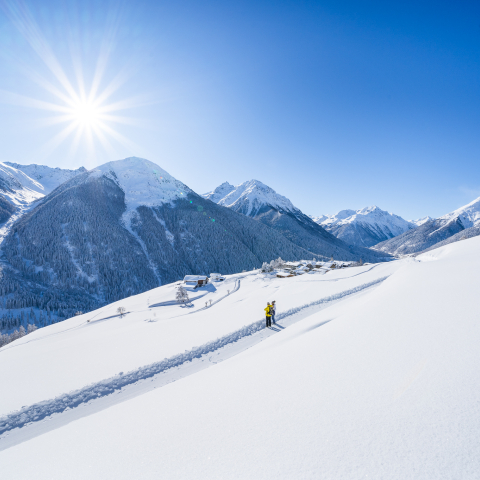 Zwei Winterwanderer auf dem präparierten Winterwanderweg der Via Engiadina mit Blick auf das verschneite Bergdorf Guarda