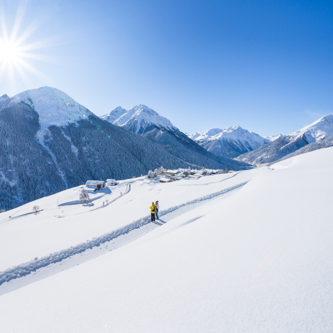 Zwei Winterwanderer auf dem präparierten Winterwanderweg der Via Engiadina mit Blick auf das verschneite Bergdorf Guarda