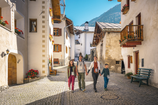 Puzzle per famiglie a Santa Maria: sulla “Chatscha jaura”, ogni indizio porta più vicino alla meta (Foto: © Svizzera Turismo / Christian Meixner) Una famiglia con due bambini passeggia nell'idilliaco villaggio di Santa Maria
