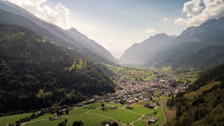 Poschiavo eingebettet in die Alpen – ein Bergdorf mit Blick auf den Lago di Poschiavo und einer malerischen Umgebung (Foto: © Marco Hartmann) Luftaufnahme von Poschiavo mit umliegender Landschaft und dem Lago di Poschiavo im Hintergrund