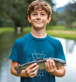 In Augio bei Pesca Sportiva fängt man sein Mittagessen selber (Foto: © Nico Schaerer) Ein Junge hält stolz eine frisch gefangene Bachforelle in beiden Händen, während er in die Kamera lächelt