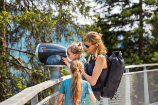 Hoch über den Bäumen – Entdeckungstour auf dem Baumwipfelpfad in Laax (Foto: © Nico Schaerer) Frau mit zwei Kindern auf dem Baumwipfelpfad Senda dil Dragun in Laax, ein Kind schaut durch ein Fernrohr