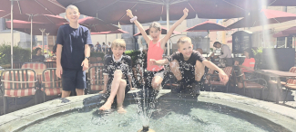 Sommerfreude am Brunnen Vier Kinder spielen lachend am Brunnen im Sonnenschein