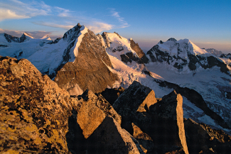 Piz Bernina with the striking Biancograt in the warm evening light over a rocky foreground
