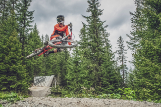 Ein Mountainbiker vollführt einen Sprung über eine Holzrampe auf der Gotschna Freeride Piste bei Klosters