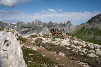 Eine Wandergruppe geniesst von einer Aussichtsplattform am Rundweg Cassons den Blick auf die markanten Felsformationen rund um Crap la Tgina.
