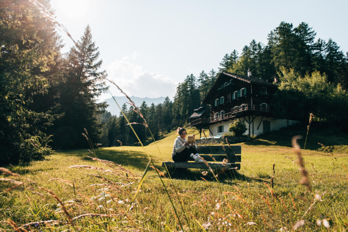 Der Hof Zuort im Unterengadin ist der perfekte Rückzugsort (Foto: © Sommertage) Bloggerin Katharina Werni liest auf einer Bank vor dem Hof Zuort in einem Buch