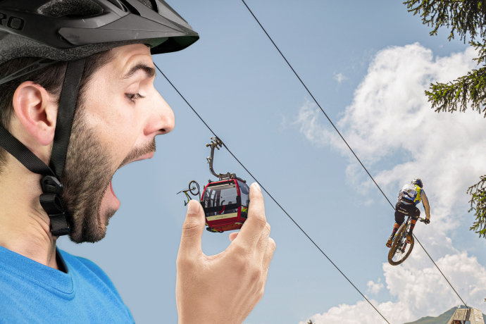 Ein übergrosser Mountainbiker beisst in die Gondel einer Bergbahn