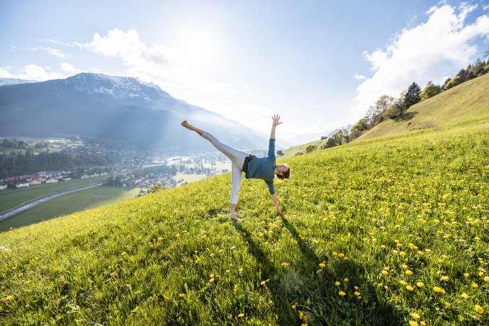 Sich frei fühlen unter freiem Himmel (Foto: © Davos Klosters / Martin Bissig) Eine Frau macht eine Yogaübung auf einer grünen Bergwiese bei Klosters