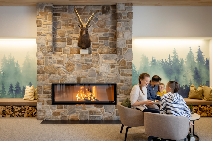 JUFA Hotel Savognin (Foto: © Harald Eisenberger) Familie sitzt an Kamin im JUFA Hotel Savognin