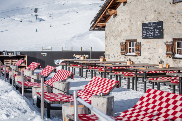 Restaurant Stalla (Foto: © Flims Laax Falera / Dani Ammann) Sonnenterrasse des Restaurants Stalla mit rot-weiss gemusterten Liegestühlen und Tischen vor verschneiter Bergkulisse