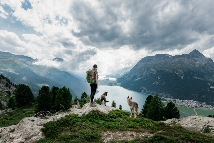 Aussicht auf die Oberengadiner Seen (Foto: © Steve Hadorn) Eine Wanderin geniesst mit ihren beiden Hunden die Aussicht auf die Oberengadiner Seenplatte