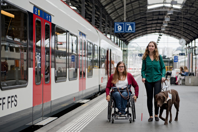 Una donna in sedia a rotelle e una donna con un cane guida sulla banchina di una stazione ferroviaria