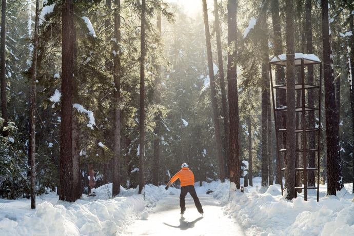With warm winter clothing, skates and a helmet, you’re perfectly equipped for the icy tour through the snowy landscape (Photo: © Nico Schaerer) A man ice skating through the winter forest on the Ice Trail Engadin