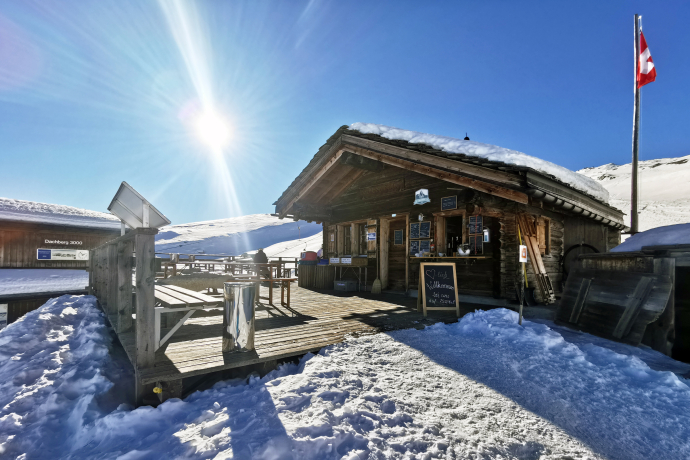 Sonnenterrasse der Dachberghütte in Vals (Foto: © Dachberghütte) Sonnenterrasse der Dachberghütte in Vals mit Holztischen und Blick auf die verschneiten Berge