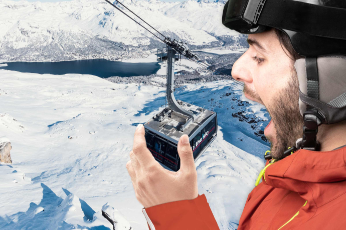 Ein übergrosser Skifahrer in voller Montur beisst spielerisch in eine Gondel einer Bergbahn