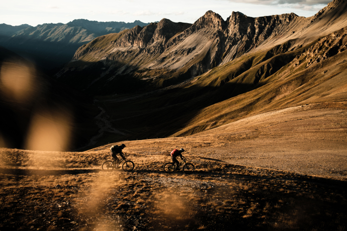 Ein Paar fährt auf Mountainbikes einen Trail in Graubünden hinunter