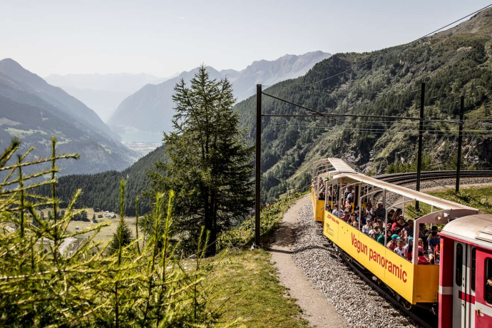 © Rhätische Bahn / Andrea Badrutt Ein offener Aussichtswagen der Rhätischen Bahn in einer Kurve mit Aussicht auf die Valposchiavo bei der Alp Grüm