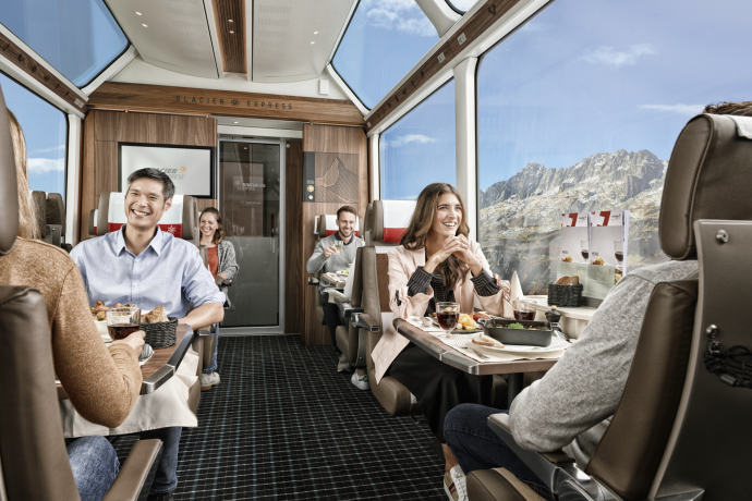 Gäste im Glacier Express lächeln sich zu und geniessen die frisch zubereiteten Speisen der Bordküche