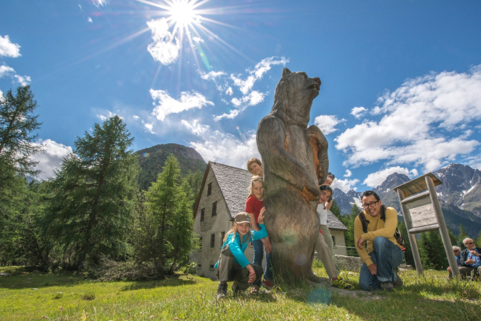 Vier Kinder stehen um eine Bärenholzfigur vor dem Museum Schmelzra S-charl