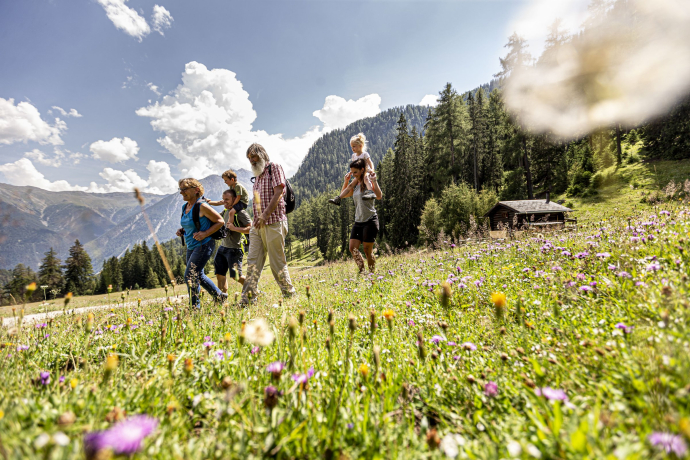 Die Nationalparkregion lädt zu spannenden Entdeckungsreisen ein (Foto: © Andrea Badrutt) Vier Erwachsene und zwei Kinder auf einer Wanderung im Engadin auf einer Blumenwiese.