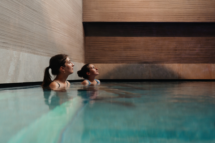 Zwei junge Frauen in einem Pool im wellnessHostel3000 Laax schauen nach oben zur Decke