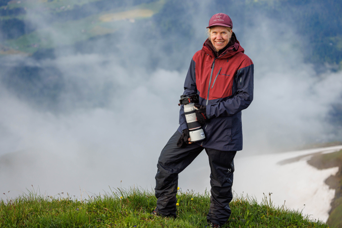 Naturfotografin Melanie Weber steht mit einer Fotokamera in den Händen auf einer Bergwiese