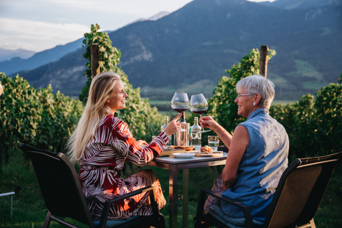 Der alte Torkel in Jenins, umgeben von Weinreben, ist ein Symbol für die lange Tradition des Weinbaus in der Bündner Herrschaft (Foto: © Heidiland Tourismus AG / Jana Figliuolo) Zwei Frauen stossen im alten Torkel in den Rebbergen von Jenins mit Rotwein an