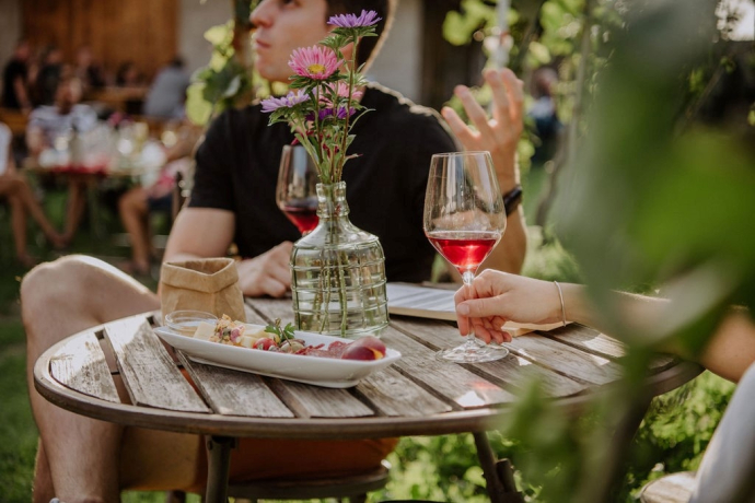 Ein junges Paar sitzt an einem kleinen Holztischchen an einem Wii-kend in Maienfeld und degustiert einen Rotwein