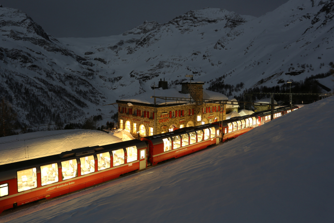 Un treno delle Ferrovie Retiche percorre, con la luna piena, il paesaggio innevato vicino all'Alp Grüm