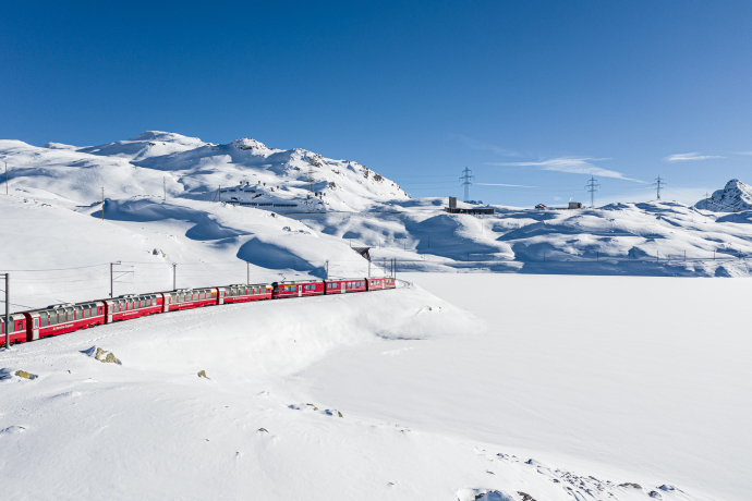 Der Bernina Express fährt im Winter entlang des Lago Bianco, umgeben von schneebedeckten Bergen und einer malerischen Winterlandschaft