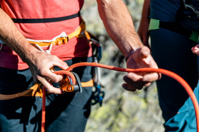 Ein Kletterer bereitet sich vor: Mit geübten Händen wird ein Knoten ins Kletterseil gemacht (Foto: © Destination Davos Klosters / Martin Bissig) Nahaufnahme eines Kletterers, der mit beiden Händen einen Knoten in ein Kletterseil bindet