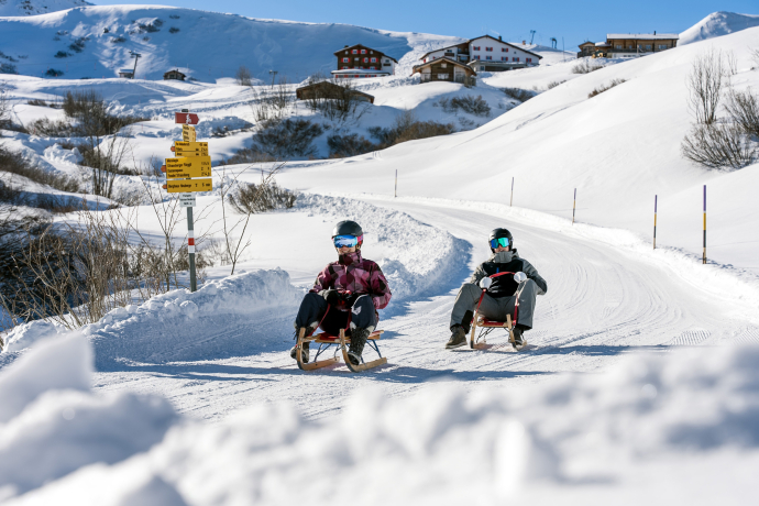 Zwei Schlittler*innen sausen die gut präparierte Schlittelpiste in den Fideriser Heubergen hinunter.