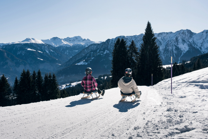 Schlittler*innen auf dem Schlittelweg Sarn geniessen das wunderschöne Bergpanorama.