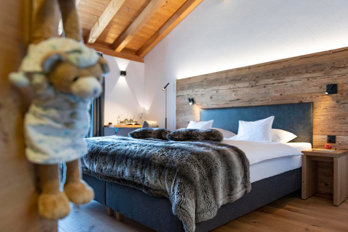 Gemütliches Zimmer im Berghotel Tgantieni, Lenzerheide, mit Holzelementen, modernem Design und einem grossen Bett mit Felldecke
