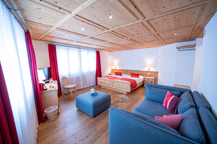 Helles, geräumiges Zimmer im Hotel Engadina, Scuol, mit viel Holz, einem grossen Doppelbett, einer blauen Couch