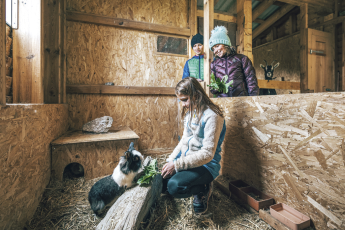 Auf Tuchfühlung mit Tieren: Kinder füttern Kaninchen auf dem Erlebnisbauernhof Pütschai Josom in Sta. Maria (Foto: © Schweiz Tourismus / Christian Meixner) Mädchen füttert ein Kaninchen in einem Stall