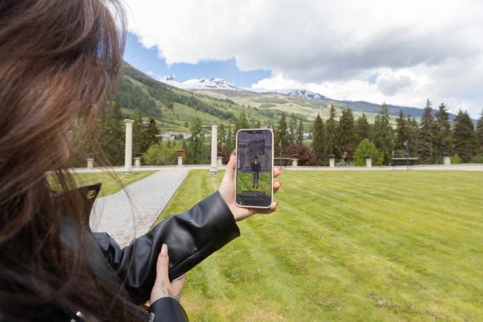 Person hält Smartphone mit AR-Figur im Kurpark Vulpera für das Rätselspiel «Misteri a Vulpera»