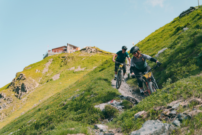Biker*innen im Trail und im Hintergrund die Hörnlihütte.