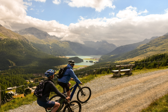 Genuss auf zwei Rädern – unterwegs auf einer kulinarischen E-Biketour im Oberengadin (Foto: © Silvan Caderas, Engadin Tourismus AG) Zwei E-Biker mit Blick auf den Silvaplanersee und das Oberengadin bei einer genussvollen Tour durch die Berge