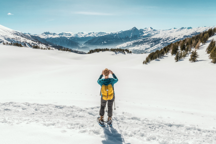 Snowshoe hiking near Feldis with a view of Piz Beverin (Photo: © Switzerland Tourism / Mattias Nutt) Snowshoe hiker with a yellow backpack stands on a snowy plain near Feldis, looking toward Brambrüesch – panoramic view in the background with the distinctive Piz Beverin