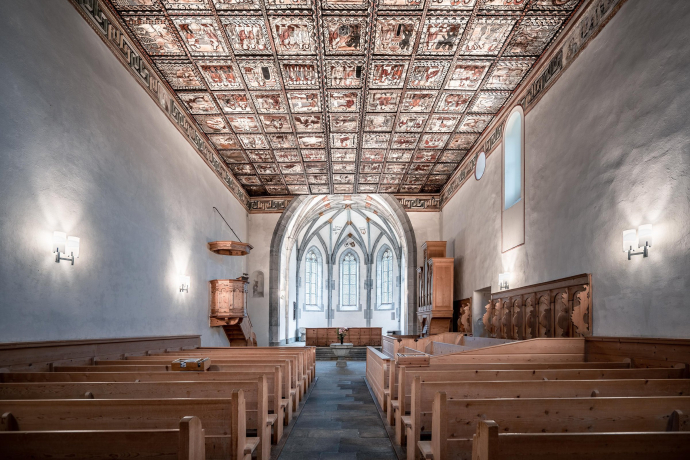 Blick ins Innere der Kirche St. Martin in Zillis mit bemalter Holzdecke und historischen Kirchenbänken