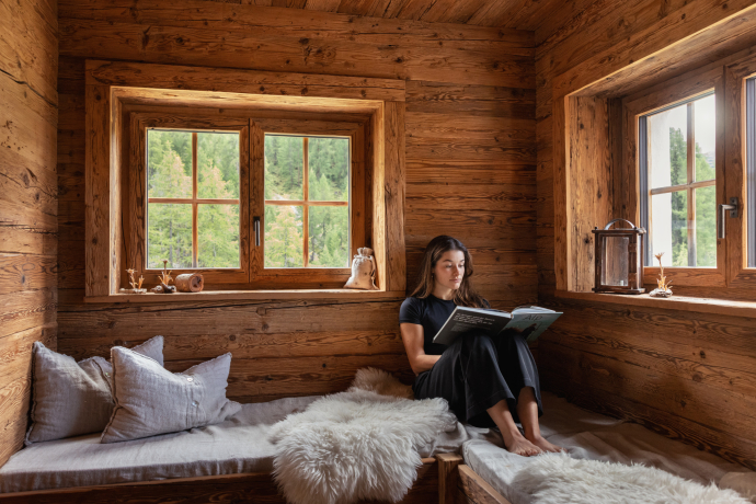 Lesepause mit Ausblick – in einem Maienäss trifft Einfachheit auf Erholung (Foto: © Schweiz Tourismus / Nico Schärer) Frau liest ein Buch in einem traditionellen Maienäss