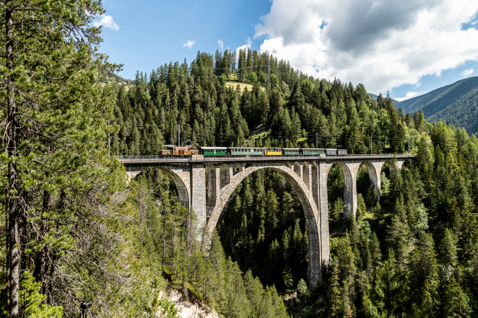Un train nostalgique de la Rhaetian Railway sur le viaduc de Wiesener, près de Davos Wiesen (© Rhaetian Railway / Andrea Badrutt) Un train historique traverse le viaduc de Wiesener, près de Davos Wiesen, au milieu d’une vallée boisée