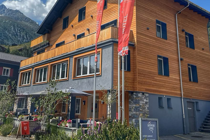 Fassade der Mountain Lodge Sedrun mit Terrasse und roten Fahnen